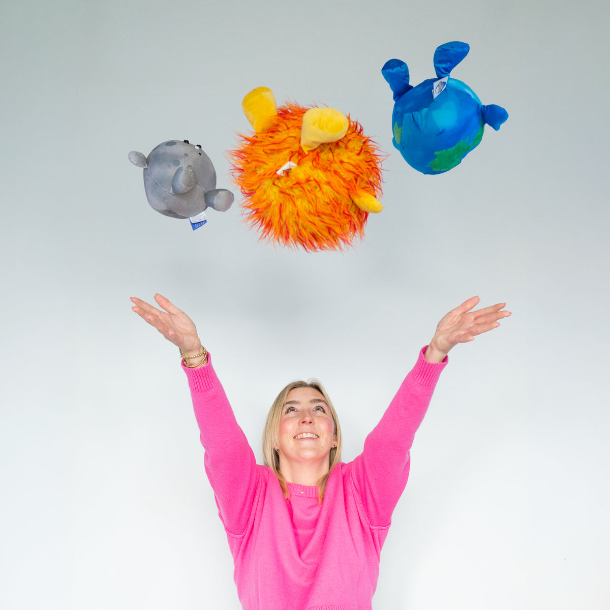Woman throwing the Earth Buddy, Sun Buddy, and Moon Buddy in the air above her head, smiling and playing with the plushies.