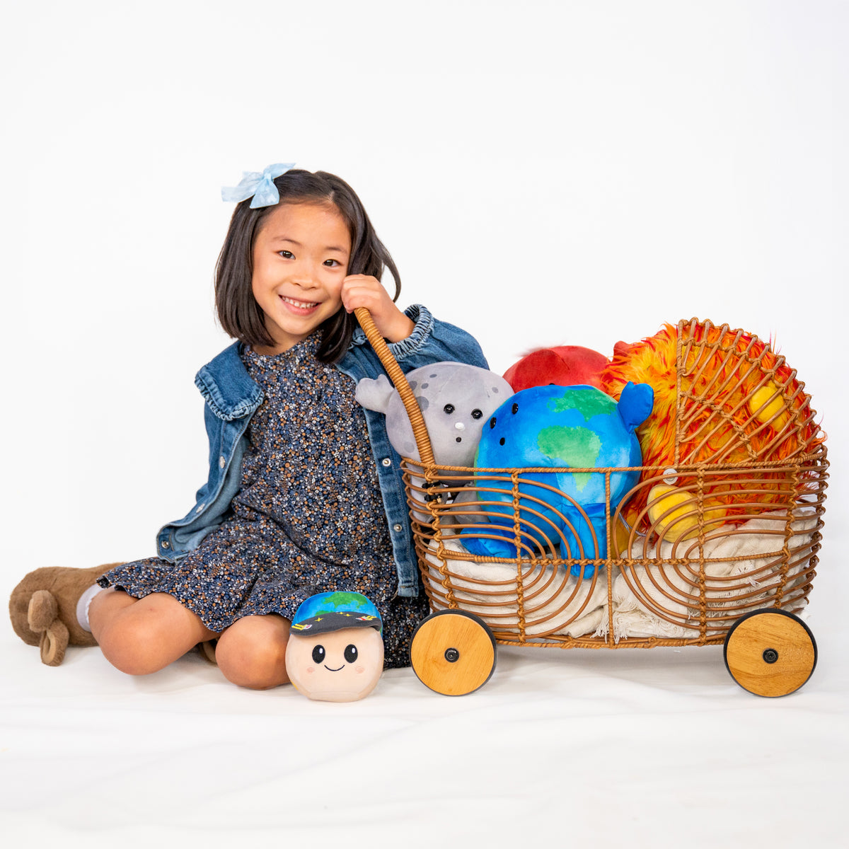 Young girl sitting on the floor with a wooden stroller filled with space plushies. Sun Buddy, Earth Buddy, Moon Buddy, Rise Buddy,  Mars Buddy