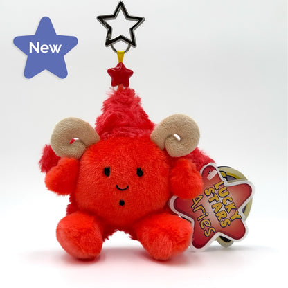 A red fuzzy keychain with tan curved horns, a red pointed hat, and a star-shaped top, shown on a white background with a hang tag that reads 'LUCKY STARS Aries'.